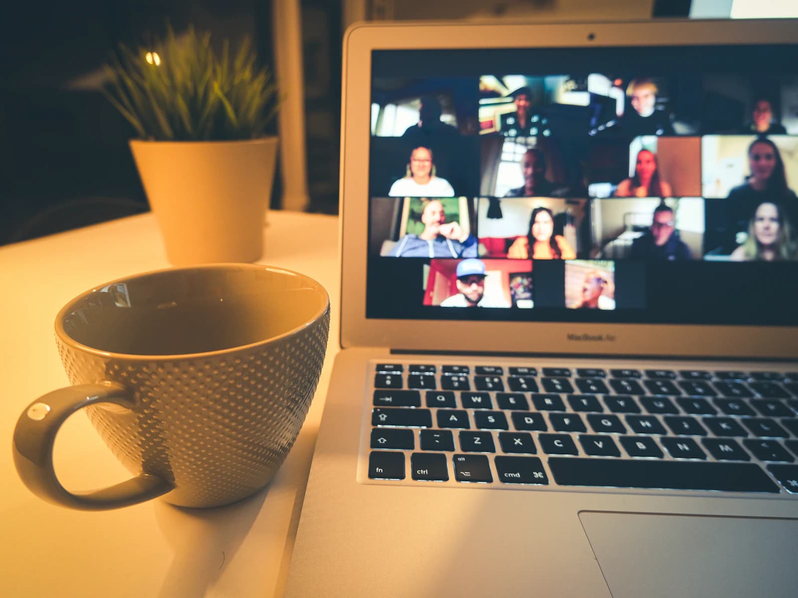 A laptop on a desk showing a video call, next to a coffee mug